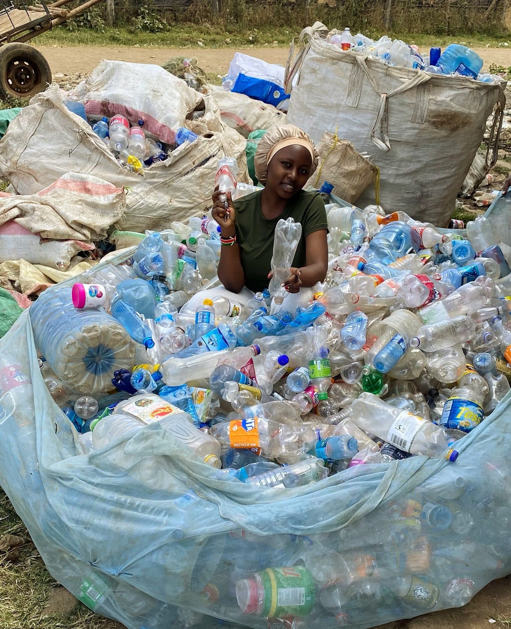 A Green Sound Solutions team member holding a recovered bottle, surrounded by sacks of collected PET awaiting sorting