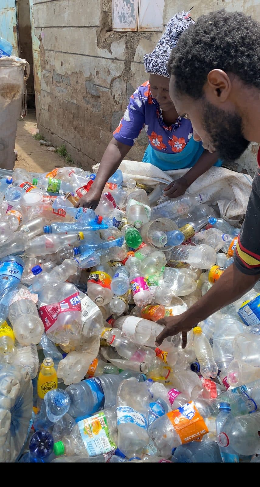 Two collectors sorting recovered plastic bottles by hand at a collection point