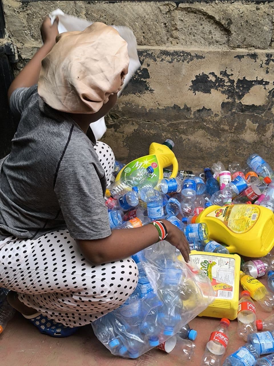 A collection partner sorting bottles by resin type against a yard wall